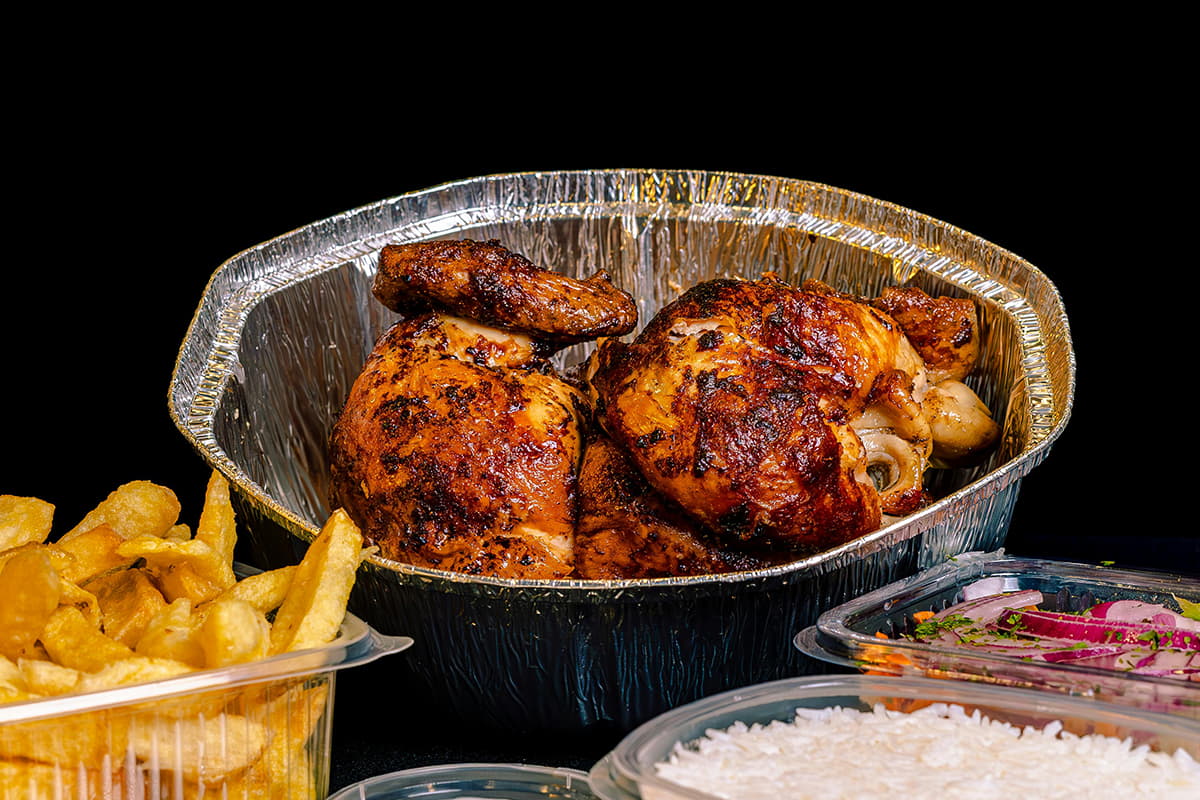 rotisserie-chicken-pieces-in-foil-container A whole rotisserie chicken in a foil takeout container surrounded by french fries and rice.