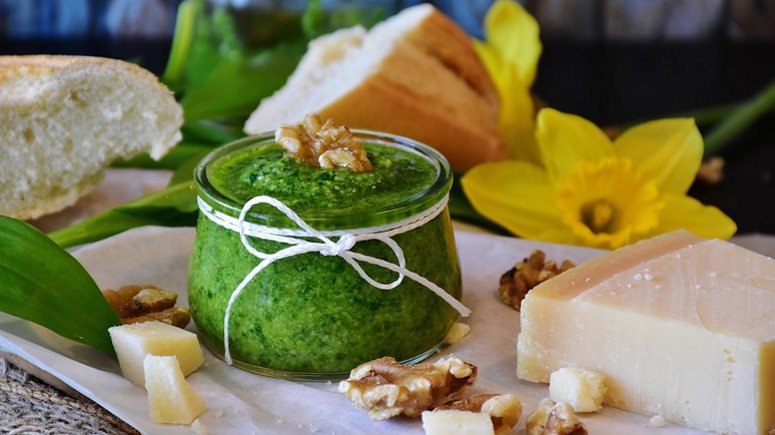 Pesto in a jar on a table surrounded by cheese and bread