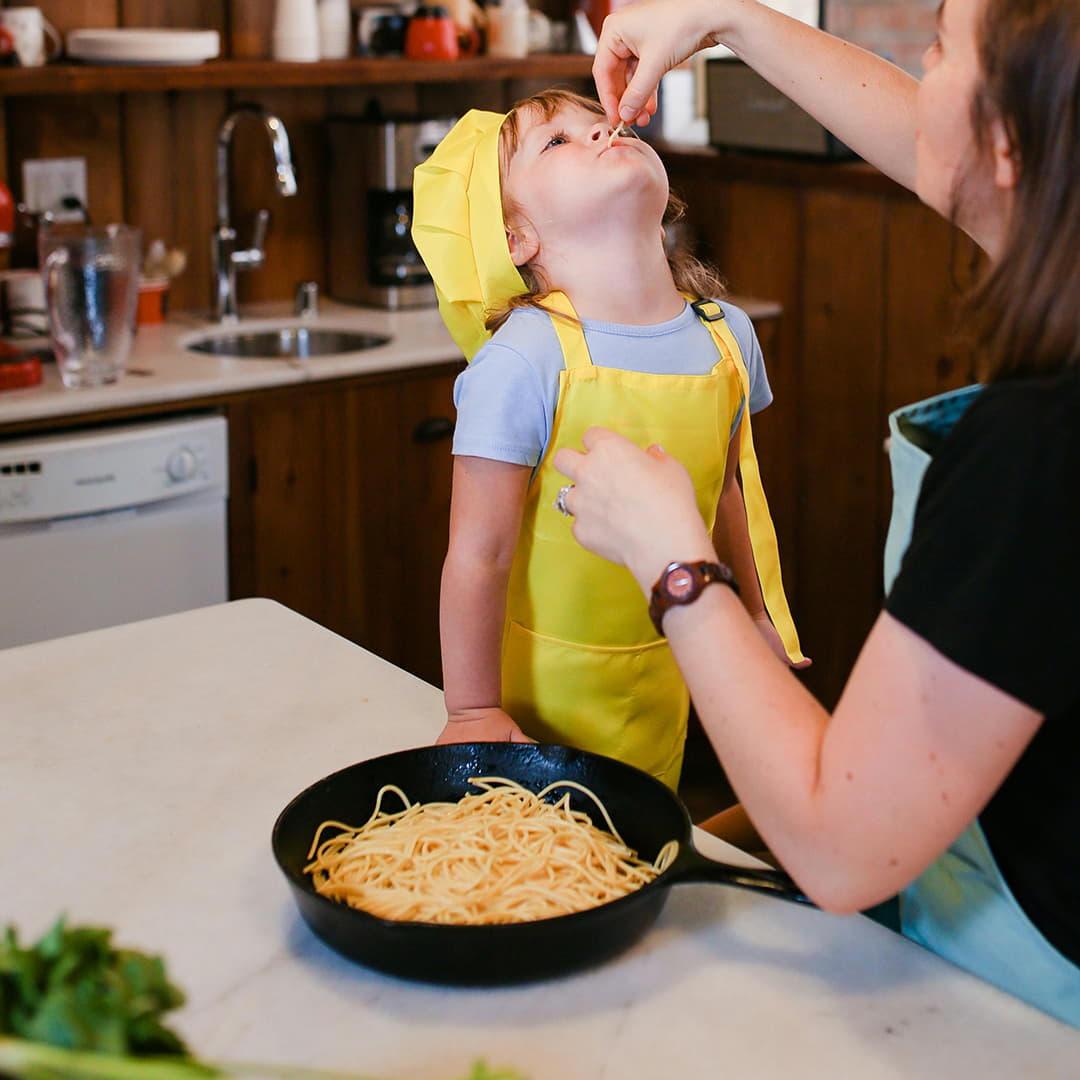 a little boy being fed reheated pasta by his mother