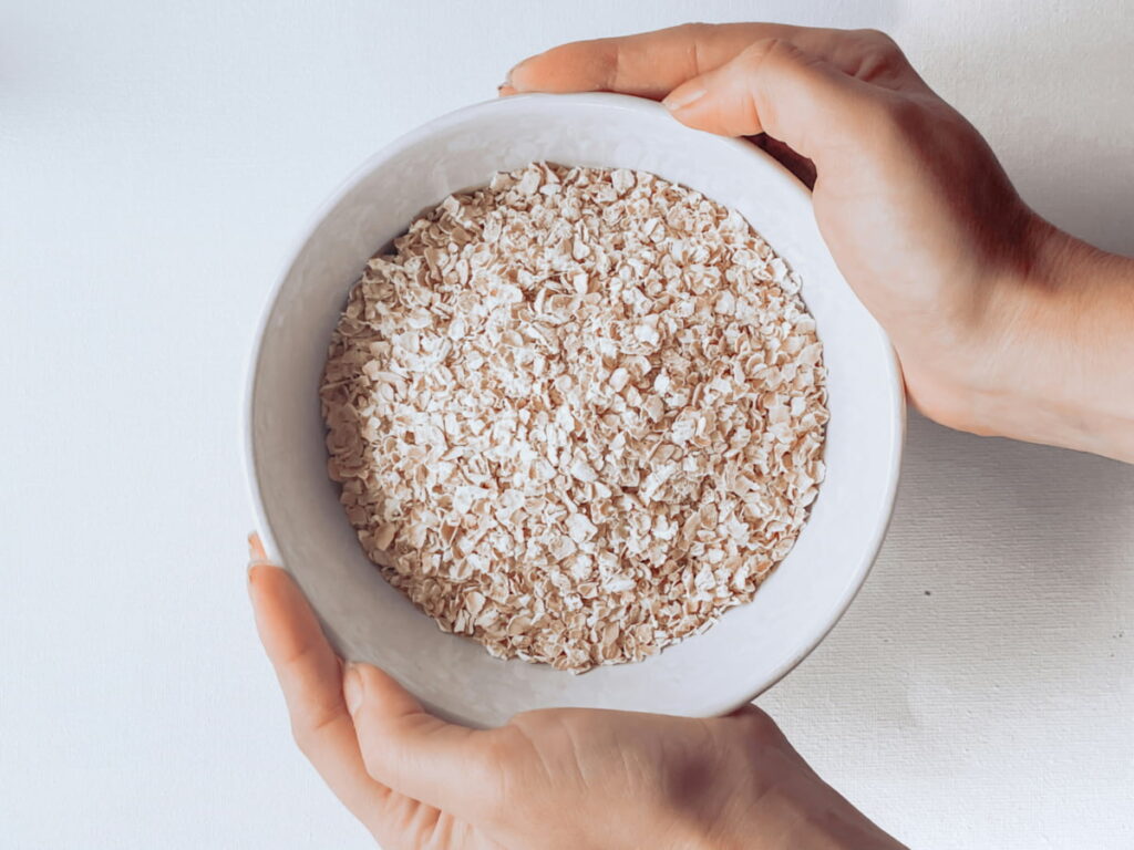 why-oatmeal-is-difficult-to-reheat Overhead shot of man holding a bowl of dry, uncooked oats.