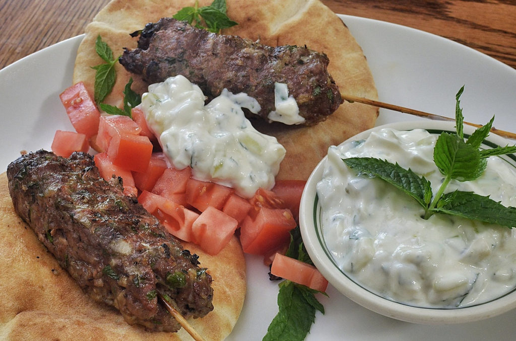 2 Gyros with Tzatziki Sauce on Them, with a bowl of tzatziki beside.