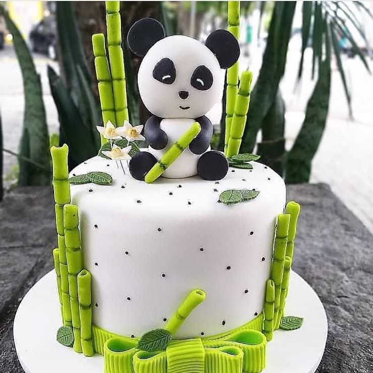 Cute panda bear sitting on top of a white cake surrounded by bamboo