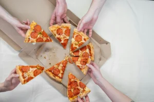 Hands grabbing slices from a large pepperoni pizza at a party table