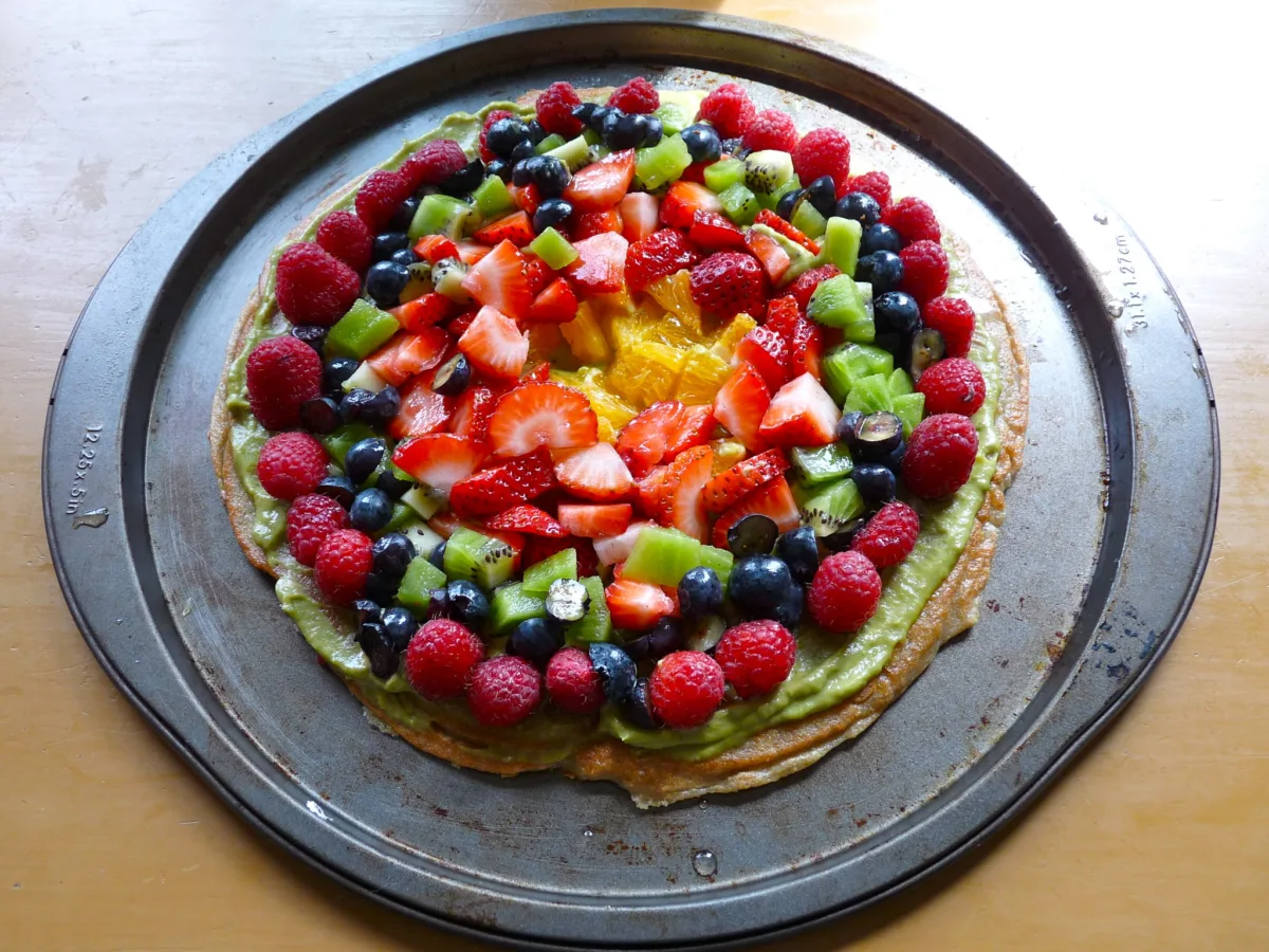 Fruit pizza made with a quinoa crust, topped with strawberries, blueberries, raspberries, kiwi and orange slices.