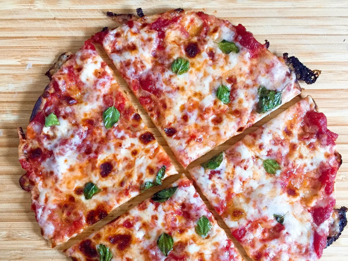 Thin flour tortilla pizza topped with melted cheese, tomato sauce and basil